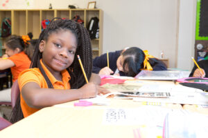 Young girl learning school routines while sitting at a desk writing with a pencil at Uplift Education in Dallas, TX