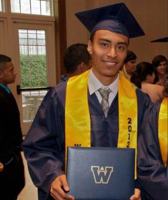 Giovanny Sanchez, A Proud Graduate In A Blue Cap And Gown, Wearing A Yellow Honor Cord, Holds A Diploma Cover With A &Quot;W&Quot; Emblem At A Crowded Graduation Ceremony. - Best Charter School Texas Education