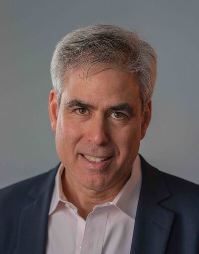 A Professional Portrait Of Jonathan Haidt, A Middle-Aged Man With Gray Hair And A Confident Smile, Dressed In A Light Blue Shirt, Posing Against A Neutral Gray Background. - Best Charter School Texas Education